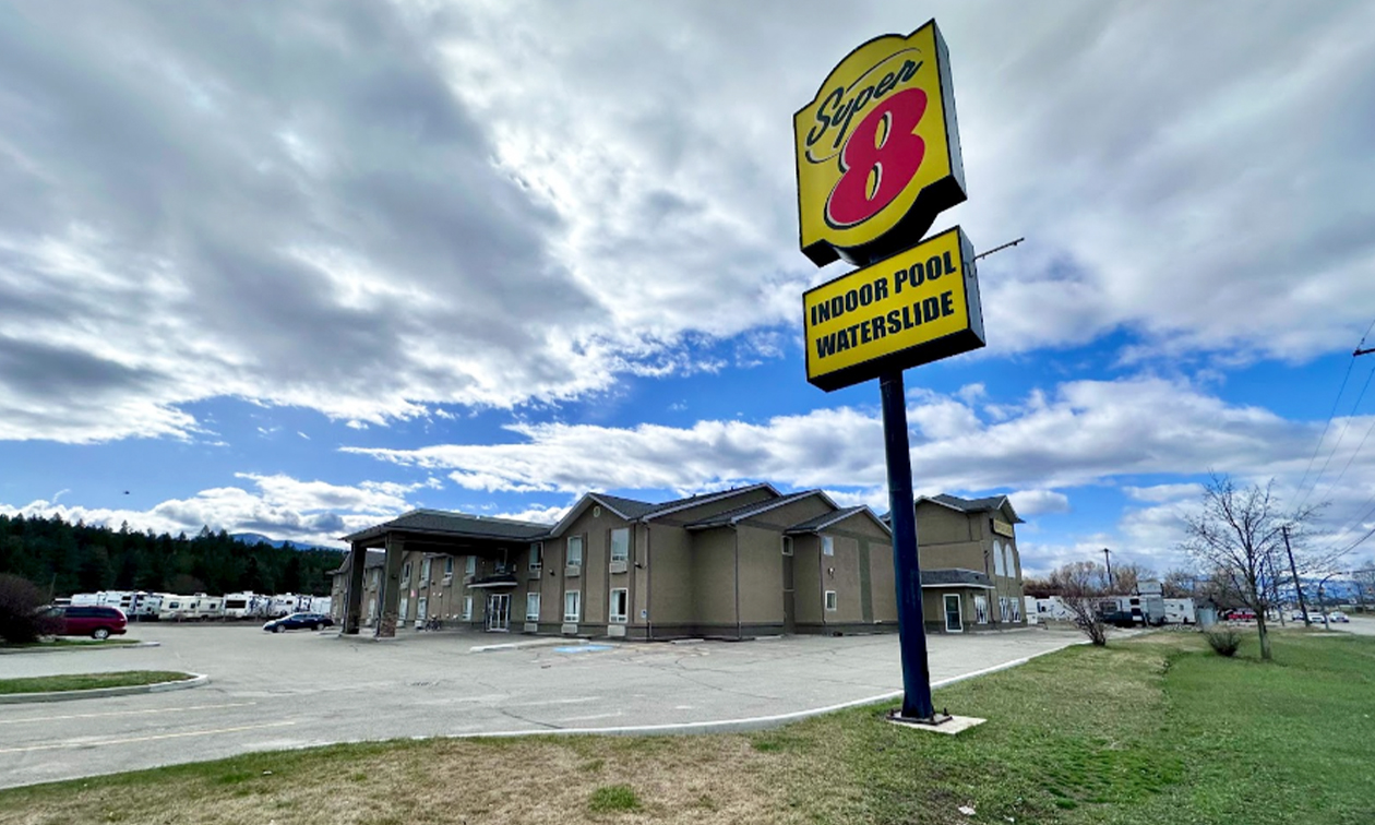 A tall sign with the Super 8 logo is in front of a large hotel with a blue sky and fluffy clouds over head.